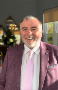 Brian Twomey, Cork wedding celebrant, smiling in a purple jacket and pink tie.