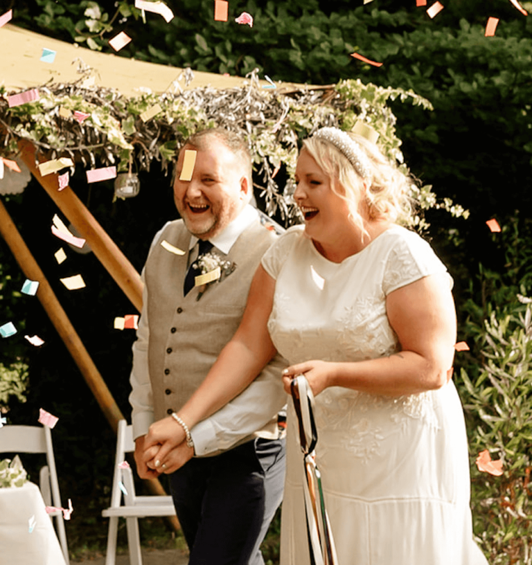 Smiling couple walking hand-in-hand under confetti after their handfasting ceremony at Barnabrow House.