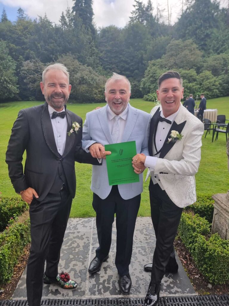 Two grooms holding their marriage certificate with their celebrant at Sheen Falls Lodge wedding.