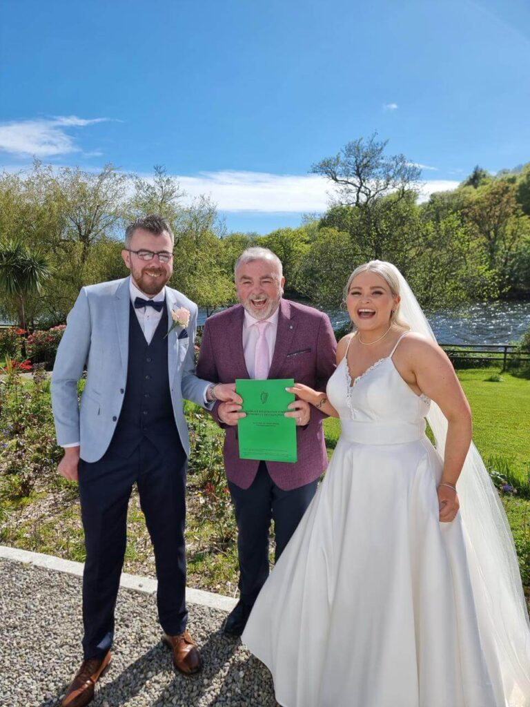 Smiling bride and groom with their celebrant holding the marriage certificate outdoors in Cork.