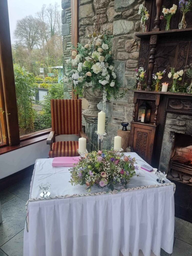 Indoor wedding ceremony setup at Muckross Park Hotel with a table adorned with floral arrangements, candles, and a handfasting cord in a rustic stone venue.