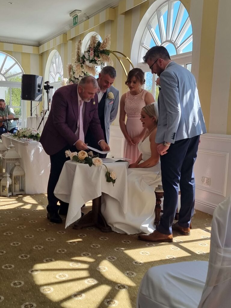 Bride and groom signing their wedding documents surrounded by the celebrant and witnesses in the sunlit ceremony venue Inishannon House Hotel.