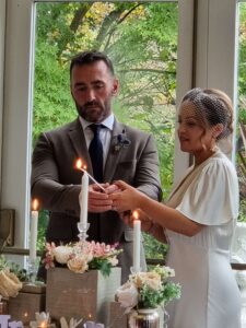 Bride and groom lighting a unity candle together during a wedding ceremony, at Seaview House, Ballylickey, wesdt Cork with floral decorations and greenery in the background.