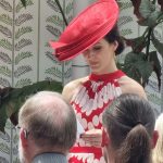 Wedding guest in a red polka-dot dress and a matching large red fascinator reading during a wedding ceremony at Ballymaloe.